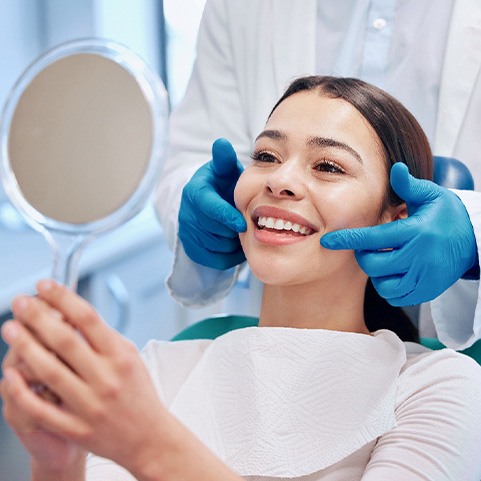Woman smiling at reflection in handheld mirror