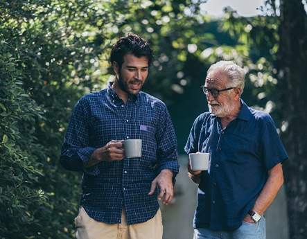 Young and older man walking and talking together outside with coffee cups