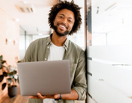 Man smiling while holding laptop in office