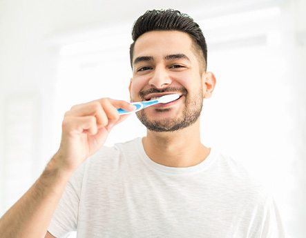 Man smiling while brushing his teeth