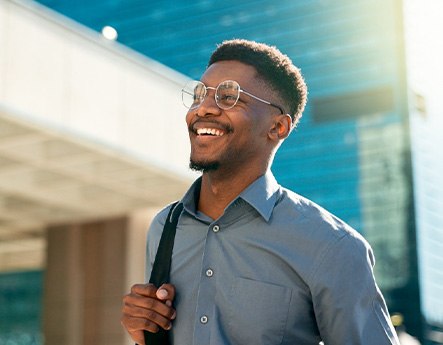 Man in glasses outside city building smiling