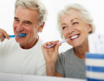 older couple brushing teeth in bathroom mirror 