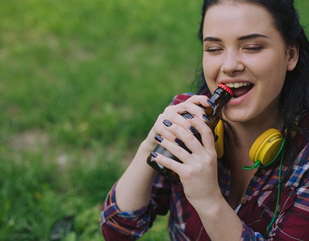 Closeup of girl in plaid shirt using teeth to open bottle cap