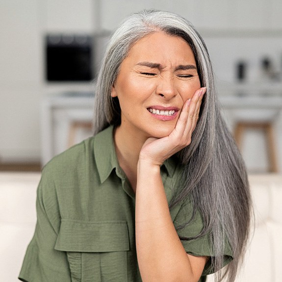 Senior woman sitting on couch rubbing jaw in pain