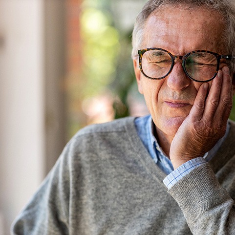 Senior man with glasses rubbing his jaw in pain