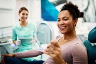 Woman looking at her smile in mirror during preventive dentistry visit