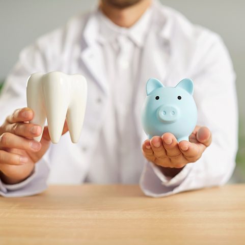 Dentist holding model tooth and blue piggy bank