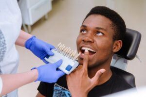 Patient pointing to teeth in dentist's chair with dentist holding veneers. 